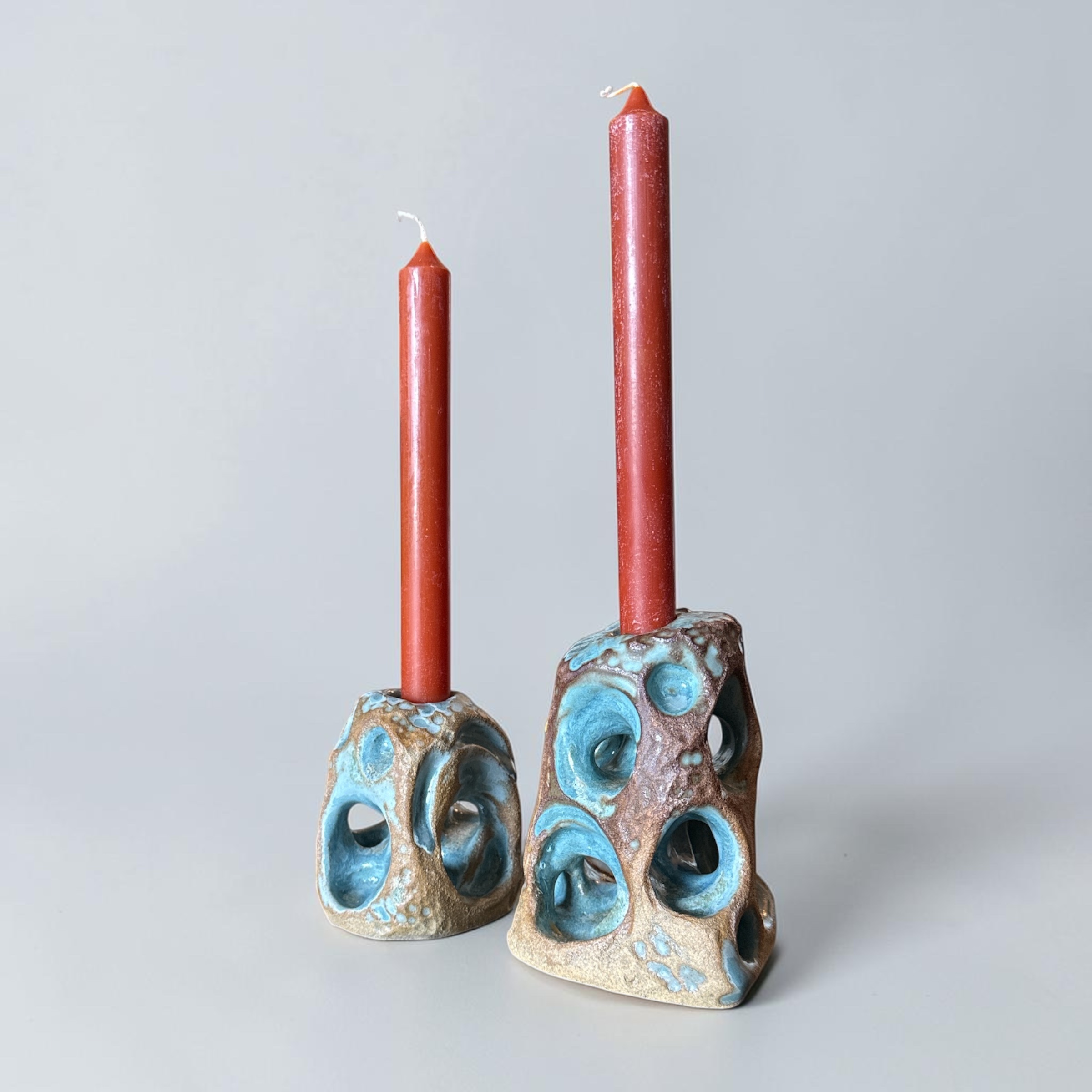 Two sculptural ceramic candle holders with turquoise openings and red candles